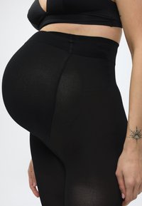 Έγκυος φοράει μαύρο κολάν εγκυμοσύνης και μαύρο αθλητικό σουτιέν, με κοντινό πλάνο στην κοιλιά και το πλάι του κορμού.