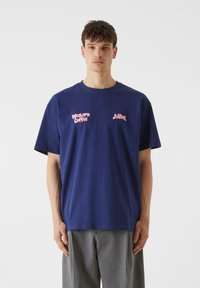 Blå bomullströja med korta ärmar, med rosa textloggor som läser "Western Coffee" och "Lishus". Enkel design, avslappnad passform.