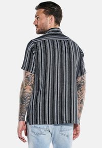 Kurzarmhemd mit vertikalen Schwarz-weiß-Streifen, Kragen und lässiger Passform, aus leichtem Stoff mit strukturierter Oberfläche.