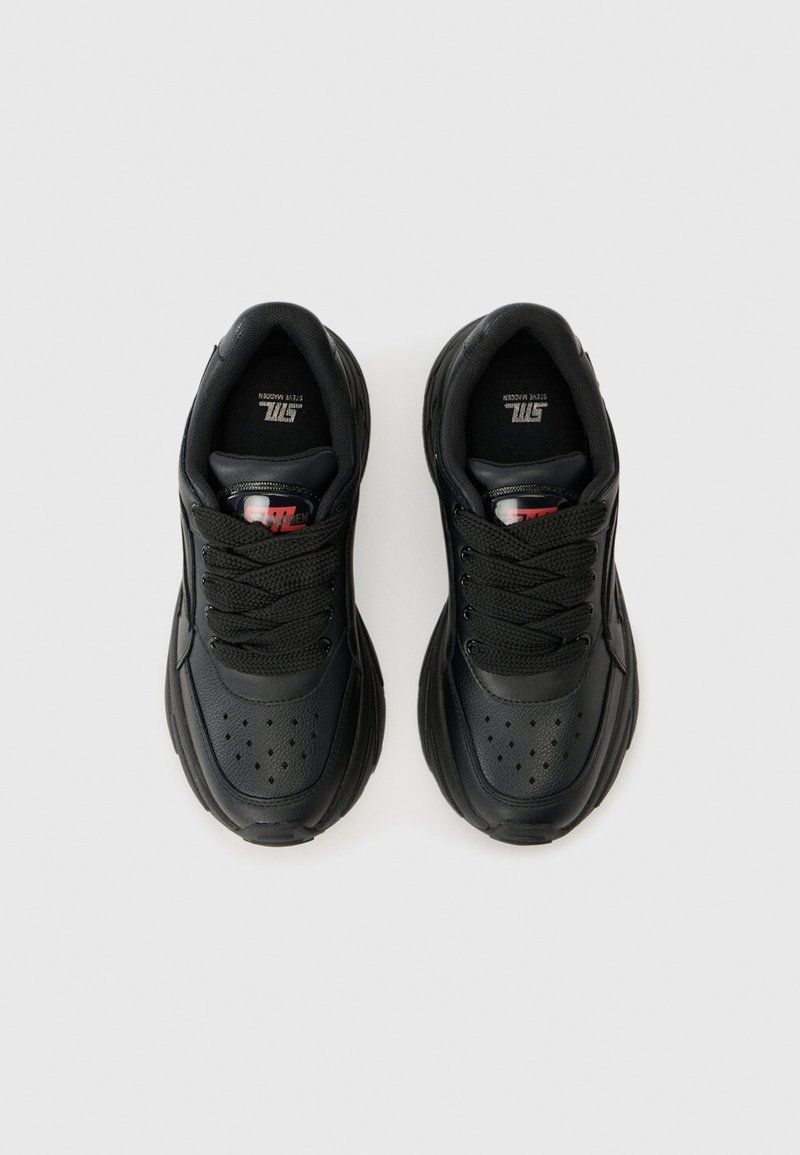 Une paire de baskets noires épaisses avec une zone de orteil perforée, des semelles épaisses et des semelles de marque présentées à plat sur un fond blanc.