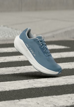 Blue Altra running shoe with white sole in mid-air above a pedestrian crossing on asphalt road.