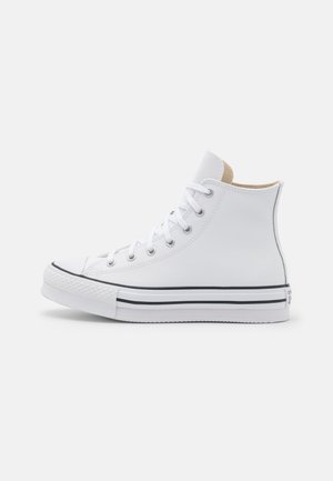 Baskets montantes blanches avec lacets blancs, bande noire sur semelle en caoutchouc blanche et œillets métalliques sur fond uni.