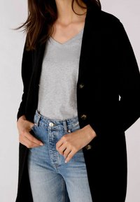 Svart cardigan med knappar, grå V-ringad t-shirt och ljusblå högmidjade jeans. Slät textur, figurnära design och avslappnad stil.