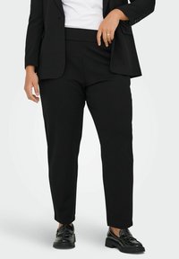 Black tapered trousers made of smooth fabric, featuring a wide waistband and side pockets, paired with polished black shoes.