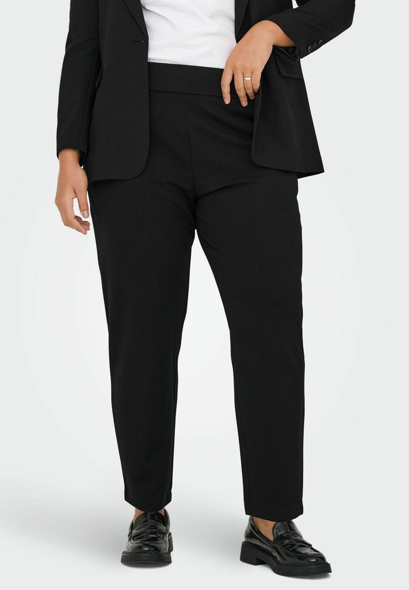 Black tapered trousers made of smooth fabric, featuring a wide waistband and side pockets, paired with polished black shoes.