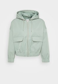 Veste cropped vert menthe avec capuche, fermeture éclair, manches élastiques et deux poches avant à rabat. Tissu lisse avec une doublure intérieure brillante.
