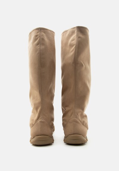 Ζευγάρι ψηλές μπεζ δερμάτινες μπότες από σουέτ που φαίνονται από πίσω με ορατές ραφές και επίπεδες λαστιχένιες σόλες.