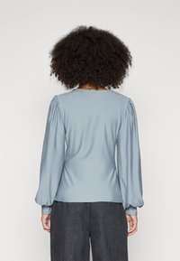 Blusa azzurro chiaro con maniche lunghe e puffate, realizzata in tessuto morbido. Presenta un collo rotondo e dettagli di cucitura sottili.