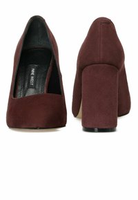 Zapatos de tacón alto de ante burdeos con diseño de punta cuadrada y tacón grueso. Etiqueta visible dentro del zapato. Textura suave.