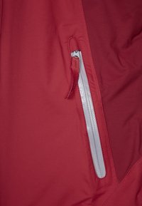 Röd ytterkläder med en elegant design, slät textur och en dragkedjeficka med grå hårdvara. Sömmarnas detaljer förstärker den strukturella integriteten.