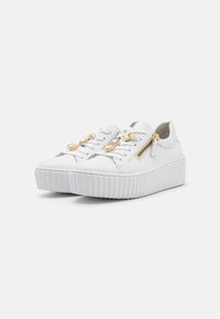 Weiße Ledersneaker mit einer Plateausohle, die goldene Verzierungen, einen seitlichen Reißverschluss und traditionelle Schnürsenkel aufweisen. Strukturiertes Sohlenmuster.