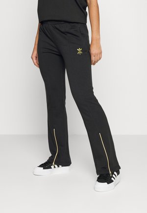 Svarta mjukisbyxor med en åtsittande design, med en guldfärgad dragkedja vid vristen och en liten gul logotyp på låret. Tillverkade av mjukt material.
