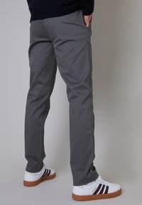 Gray cotton trousers paired with white sneakers featuring brown accents and dark stripes. Trousers have a straight-cut and side pockets.