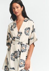 Květinové kimono šaty ve světlé krémové barvě s námořnickými a oranžovými květinovými vzory, s výstřihem do V a vázaným pasem. Krátké rukávy.