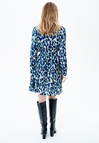 Vestido con estampado floral en tonos azules y verdes, cintura ceñida, mangas largas, falda de volantes, combinado con botas negras hasta la rodilla.