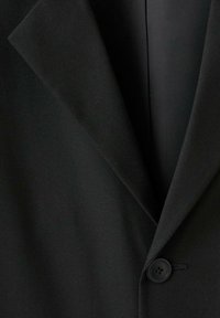 Blazer nero con colletto a revers, chiusura a un bottone, texture del tessuto liscia e struttura sartoriale con linee pulite.