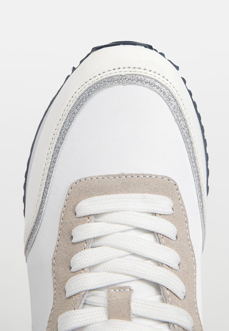 Sneaker bianco con una parte superiore testurizzata, accenti in suede grigio e un bordo di glitter argento lungo i lati. I lacci sono in evidenza.