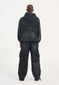 Sudadera negra de gran tamaño con un intrincado gráfico gris en la espalda, combinada con pantalones cargo sueltos que presentan un diseño de dragón bordado.