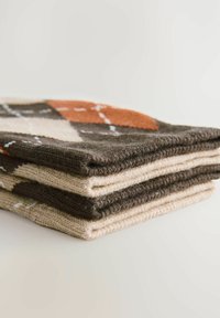 Gestapelte gestrickte Decken mit Mustern in dunklem Braun, Beige und Orange. Auffällige Diamant- und Kreuzmuster auf strukturiertem Stoff.