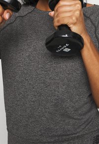 Musta käsipainot pidetään käsissä, yllään tummanharmaa tekstuuriurheilu t-paita, jossa on lyhyet hihat ja pyöreä pääntie.