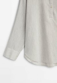 Chemise beige clair à manches longues avec fines rayures verticales, poignet boutonné et détail arrondi sur l'ourlet sur fond blanc uni.