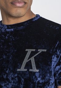 Námořnická sametová mikina s texturovaným povrchem a stříbrným kamínkovým logem 'K' na hrudníku. Design s kulatým výstřihem a krátkými rukávy.