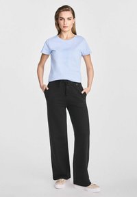 Jasnoniebieska koszulka z krótkim rękawem w połączeniu z czarnymi, szerokimi spodniami dresowymi z elastycznym paskiem w talii i bocznymi kieszeniami. Neutralne buty z płótna.