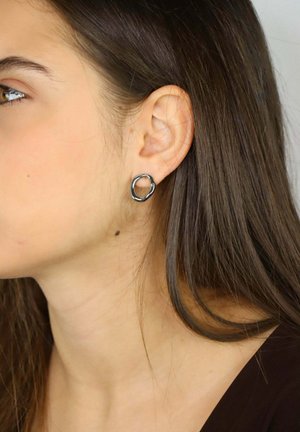 Srebrna kolczyk kołowy na modelce, o gładkiej, lekko nieregularnej powierzchni i minimalistycznym designie, noszony na lewym uchu.