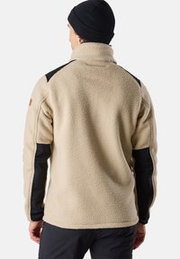Beige fleece jacket with a high collar, black shoulder accents, and black sleeve panels. Soft texture and relaxed fit.
