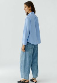 Lichtblauw gestreepte overhemd met lange mouwen, gecombineerd met losse lichtblauwe jeans en zwarte instap schoenen.