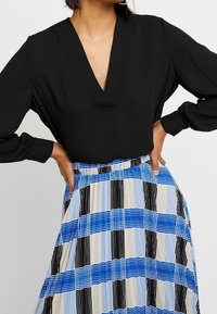 Black long-sleeve blouse with a deep V-neck, paired with a pleated, striped skirt in blue, black, and beige hues. Elastic waistband detail.