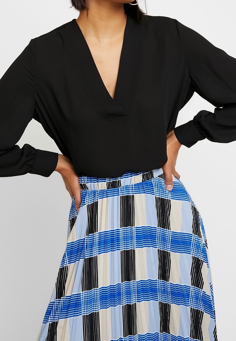 Black long-sleeve blouse with a deep V-neck, paired with a pleated, striped skirt in blue, black, and beige hues. Elastic waistband detail.