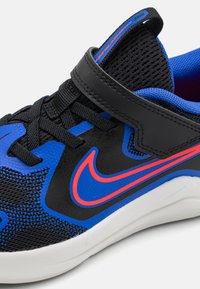 Chaussure de sport noire et bleue avec un dessus en maille, sangle ajustable, accents réfléchissants rouges et semelle en caoutchouc blanc.
