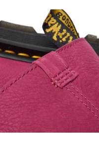 Gros plan sur le talon d'une chaussure en cuir bordeaux avec une couture détaillée et une languette en tissu noire et jaune avec logo.