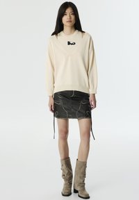 Krémový oversized svetr s výřezy, kombinovaný s černou riflovou mini sukňou s bílým prošitím a kapsami. Suede vysoké boty po kolena.
