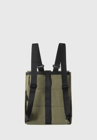Sac olive avec des sangles noires réglables, présentant une texture matelassée, une poche zippée sur le côté et des accents en sangle noire au centre.