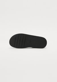 Zwarte rubberen zool met een gestructureerd oppervlak, voorzien van horizontale groeven voor grip en een ronde neus. Eenvoudig ontwerp zonder extra accenten.