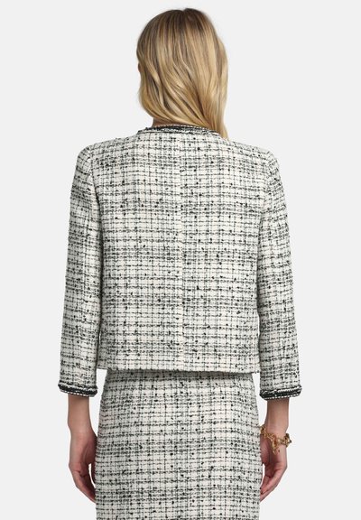Tvid jakna v tkalni tehniki v beli in črni barvi s kvadratnim krojem, rokavi do komolcev ter kontrastnim robom ob manšetah in ovratniku.