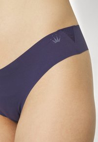 Sous-vêtements bleu marine avec une texture lisse, présentant une coupe triangulaire et un détail subtil du logo de couronne sur un côté.