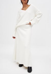 Maglione bianco a coste con scollo a V e maniche lunghe abbinato a una gonna maxi coordinata. Mocassini neri completano il look.