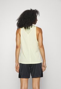 Top atlético sin mangas de color amarillo claro con un diseño de espalda en forma de V, combinado con pantalones cortos negros, fabricado con material transpirable y un ajuste relajado.