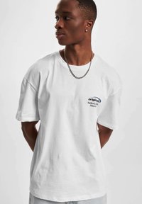 Hvit bomull t-skjorte med korte ermer, rund hals, og et fronttrykk med "originals" og "Surfers Crew Since" i mørkeblå farge.