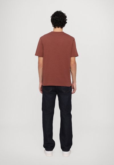 T-shirt marron à manches courtes, en coton, coupe droite. Associé à un jean en denim bleu foncé, coupe détendue, avec des détails de couture subtils, et des chaussures blanches.