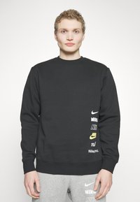 Felpa nera con collo a giro e maniche lunghe, con diversi loghi Nike bianchi e gialli sul lato sinistro. Tessuto morbido.