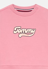 Růžový svetr s žebrovaným výstřihem a manžetami, s výrazným vyšitým logem "Tommy" a detailem "CLASS OF 1985".