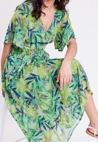 Robe maxi verte en tulle avec des motifs de feuilles et de fleurs. Elle présente un décolleté en V, des manches volantées et une taille cintrée, améliorant la circulation de l'air et le confort.