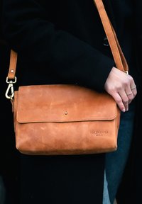 Brown leather shoulder bag with a fold-over flap, metal snap closure, and adjustable strap. Features embossed "HOLZRICHTER BERLIN."
