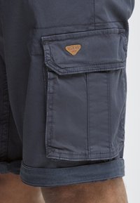 Laivaston cargo shortsit, joissa on käännetyt helmat, ja joissa on suuri sivutasku sekä vaalea logo-patch. Valmistettu kevyestä kankaasta, jossa on sileä rakenne.