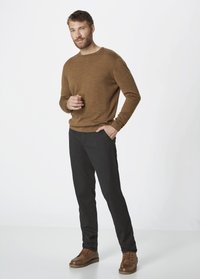Brown knitted sweater, gray tailored pants, and brown leather shoes. Model stands with one hand in pocket, neutral background.
