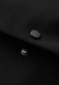 Tissu noir avec deux boutons-pression noirs, un mâle et une femelle, partiellement connectés.